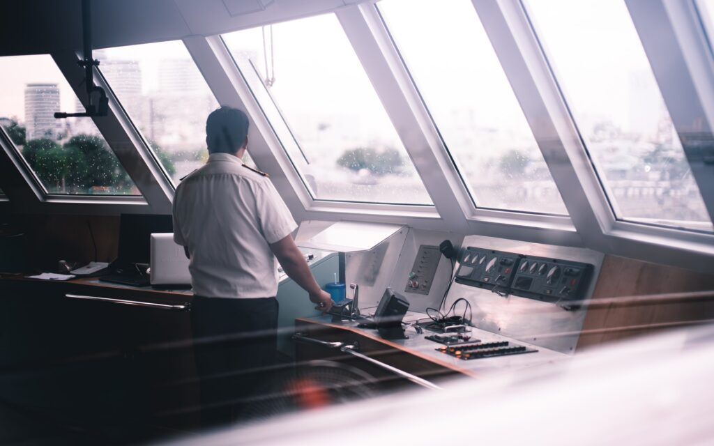 Image description: A uniformed seafarer at the controls of a ship, looking out the front windows. End of alt text.