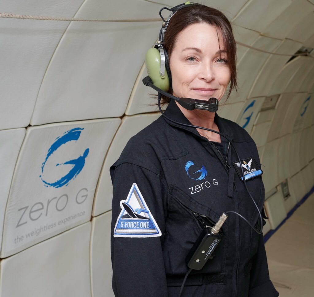 Image description: A portrait of Michelle Peters, wearing a Zero-G branded jumpsuit and headset, inside a Zero-G plane. End of alt text.