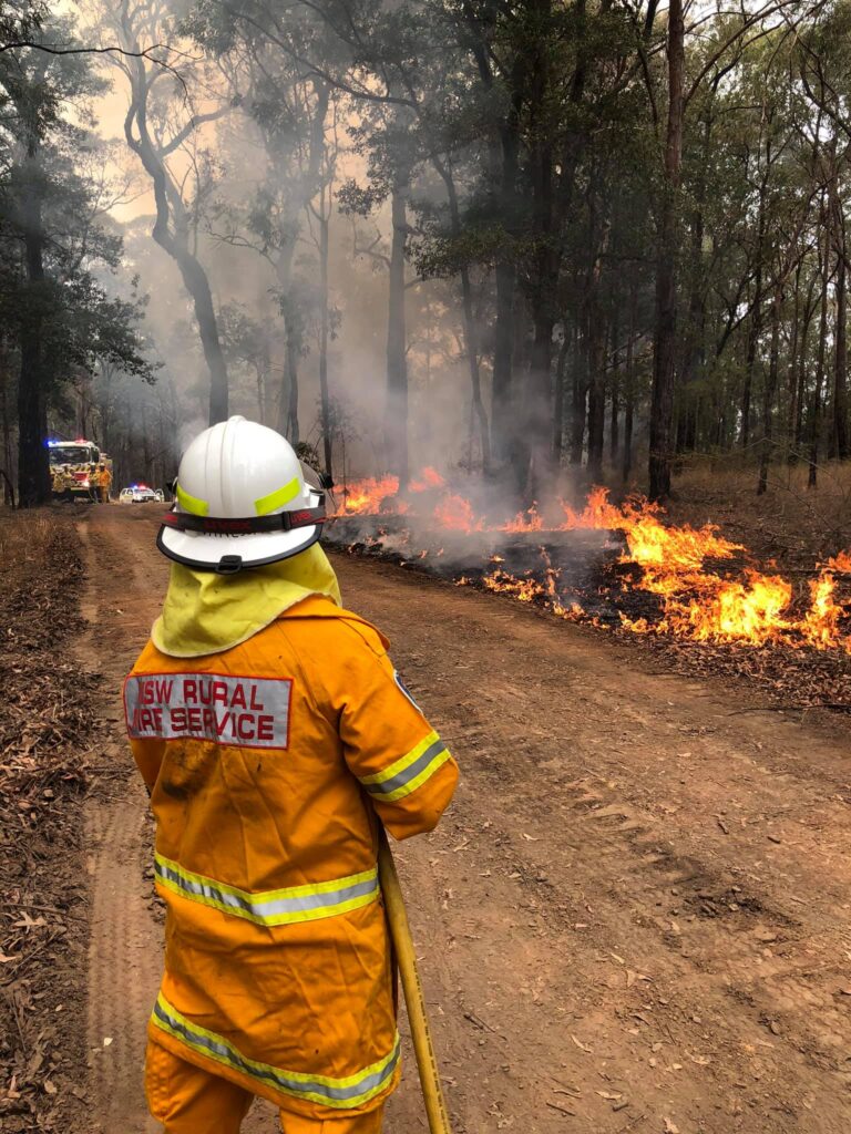 a woman in fire fighter gear aims a hose at a wildfire in Australia.